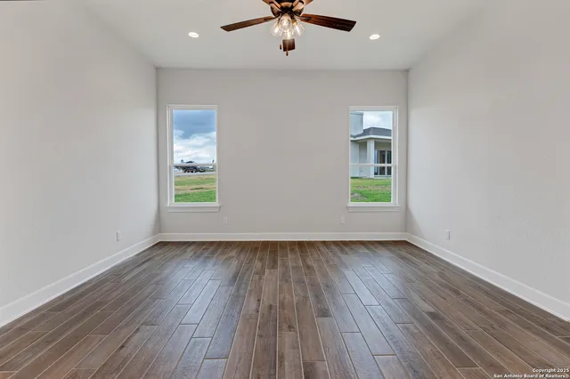 an empty room with wooden floor chandelier fan and windows