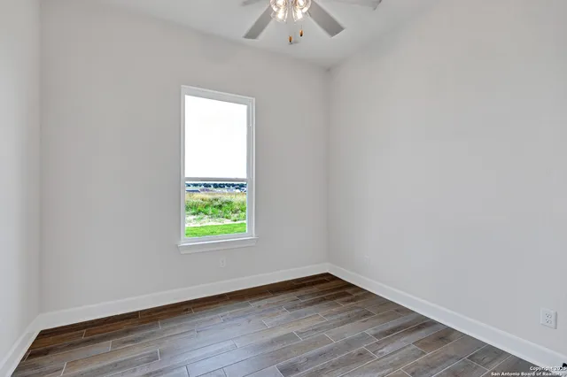 an empty room with wooden floor a chandelier fan and windows