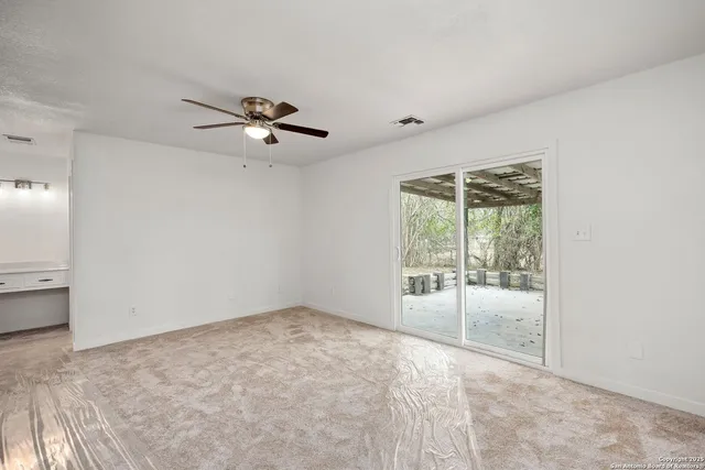 an empty room with chandelier fan and windows