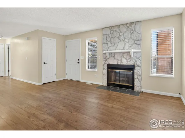 a view of an empty room with wooden floor fireplace and a window