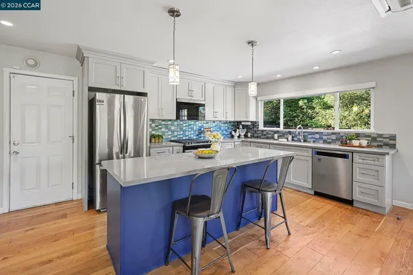 a kitchen with stainless steel appliances a dining table chairs refrigerator and cabinets