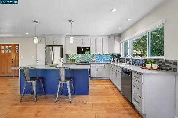 a kitchen with stainless steel appliances kitchen island granite countertop wooden cabinets a stove a sink dishwasher and a dining table with wooden floor