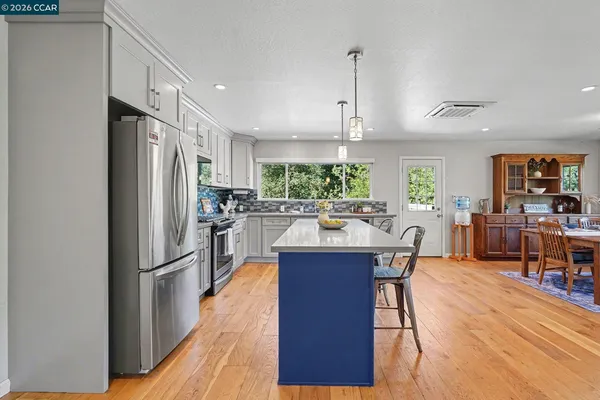 a kitchen with stainless steel appliances granite countertop a refrigerator a sink dishwasher a stove and a dining table with wooden floor