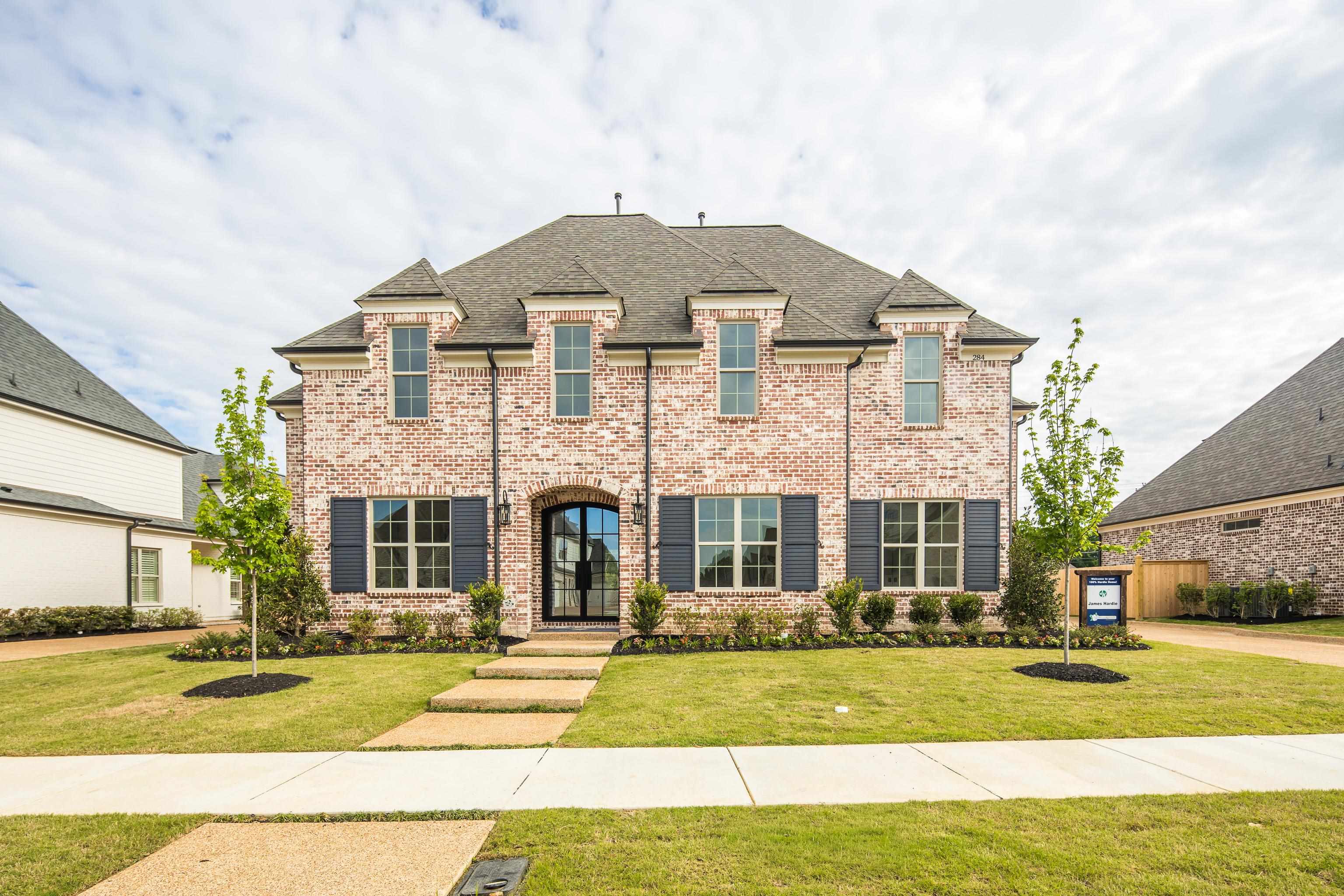 284 Keisie Lane Collierville, TN 38017 - Photo 3 of 34 Distinguished two-story brick residence featuring a charcoal shingle roof, dark shutters, and an arched entry door