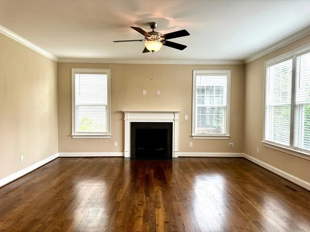an empty room with wooden floor a ceiling fan and windows