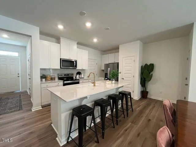 a kitchen with stainless steel appliances granite countertop a stove top oven a refrigerator a sink and white cabinets with wooden floor