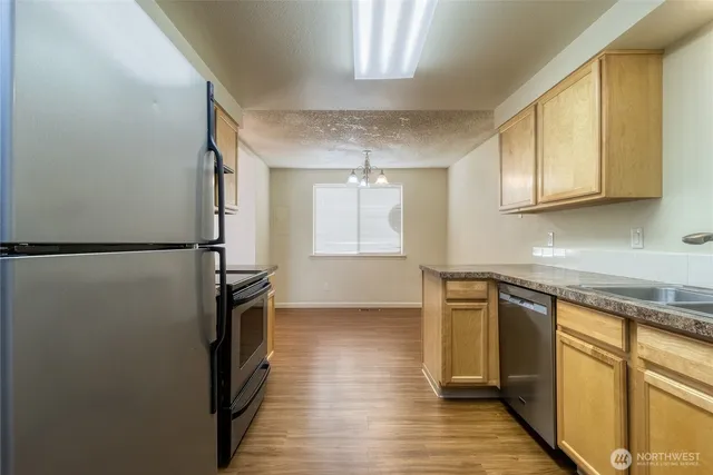 a kitchen with stainless steel appliances granite countertop a refrigerator a sink dishwasher a stove and white countertops with wooden floor