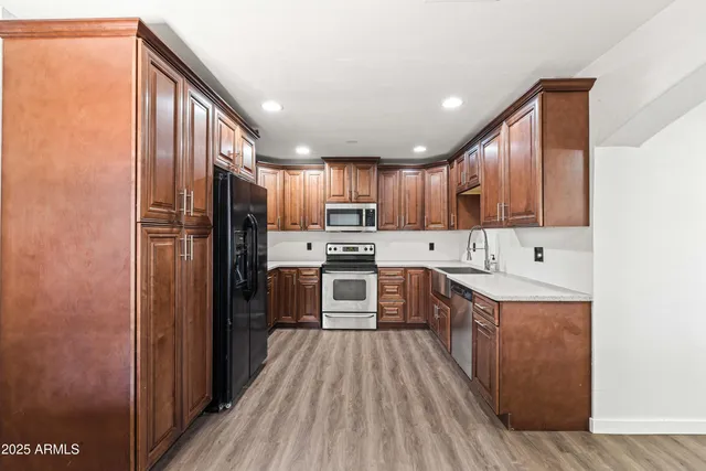 a kitchen with stainless steel appliances granite countertop a refrigerator a stove top oven a sink and dishwasher with wooden floor