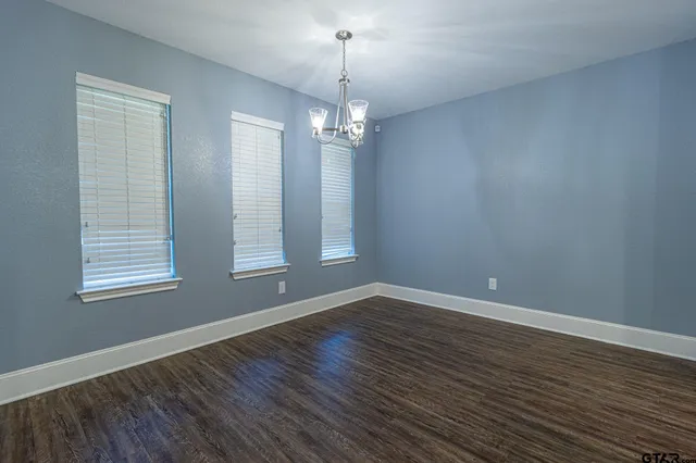 an empty room with wooden floor chandelier and windows