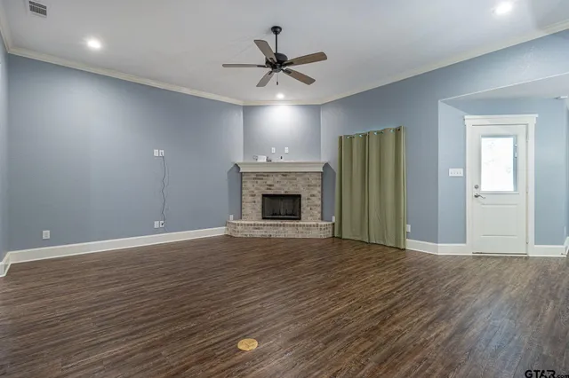 an empty room with wooden floor a ceiling fan a fireplace and windows