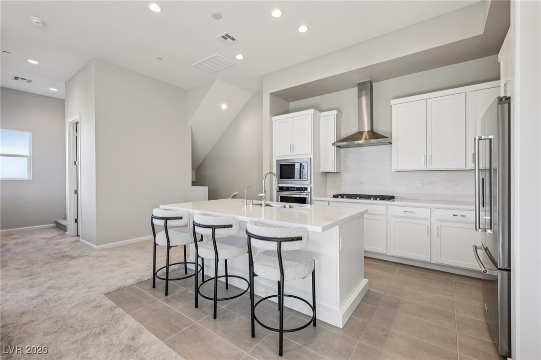 3338 Esker Rdg Avenue Henderson, NV 89044 - Photo 14 of 84 Kitchen featuring a breakfast bar, wall chimney exhaust hood, a kitchen island with sink, white cabinetry, and recessed lighting