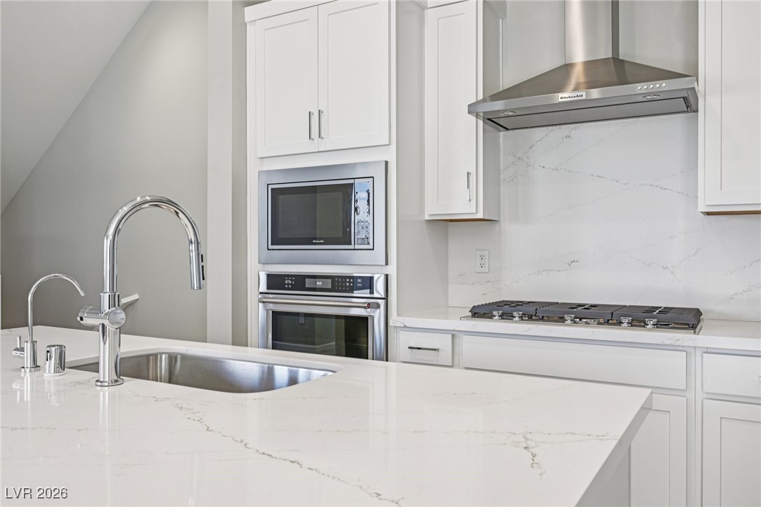 3338 Esker Rdg Avenue Henderson, NV 89044 - Photo 15 of 84 Kitchen featuring white cabinetry, wall chimney range hood, appliances with stainless steel finishes, and light stone counters