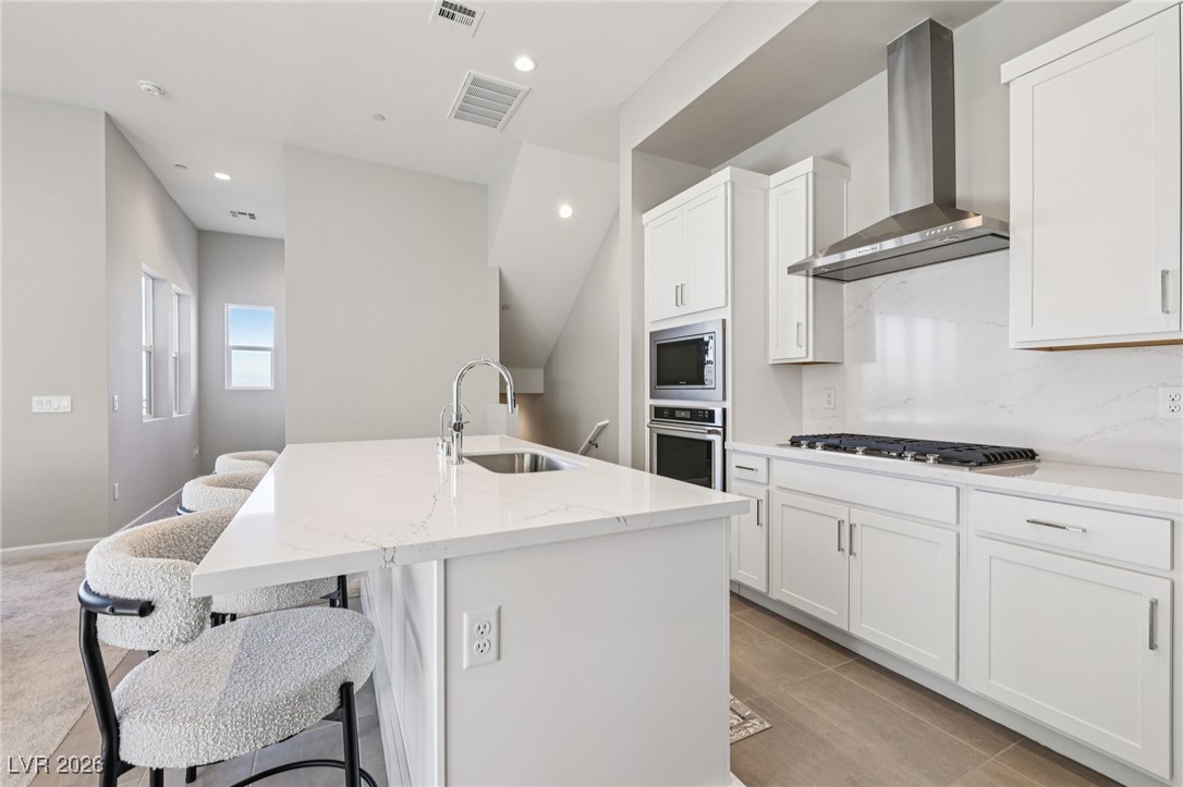 3338 Esker Rdg Avenue Henderson, NV 89044 - Photo 17 of 84 Kitchen with wall chimney range hood, a breakfast bar area, white cabinetry, stainless steel appliances, and an island with sink