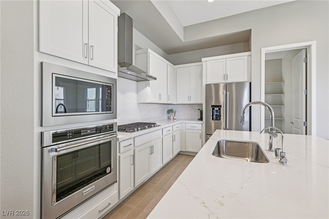 3338 Esker Rdg Avenue Henderson, NV 89044 - Photo 19 of 84 Kitchen with stainless steel appliances, wall chimney exhaust hood, light stone counters, and white cabinets