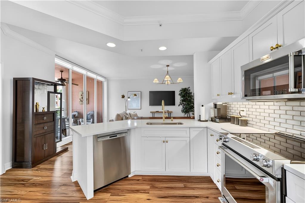 450 Bayfront Place, Unit 4202 Naples, FL 34102 - Photo 2 of 39 Kitchen with a peninsula, stainless steel appliances, white cabinets, crown molding, and tasteful backsplash