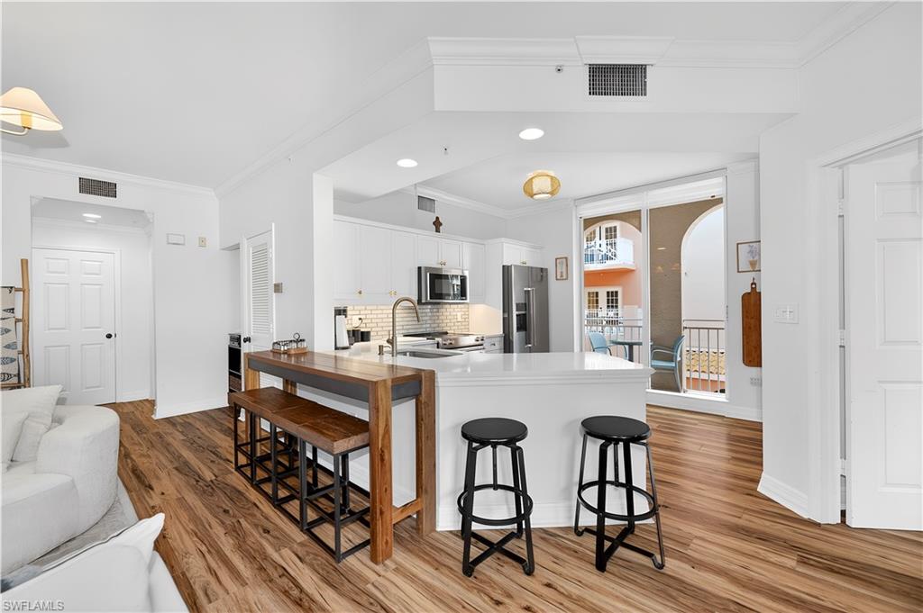 450 Bayfront Place, Unit 4202 Naples, FL 34102 - Photo 4 of 39 Kitchen featuring crown molding, white cabinets, a kitchen breakfast bar, a peninsula, and light wood-type flooring