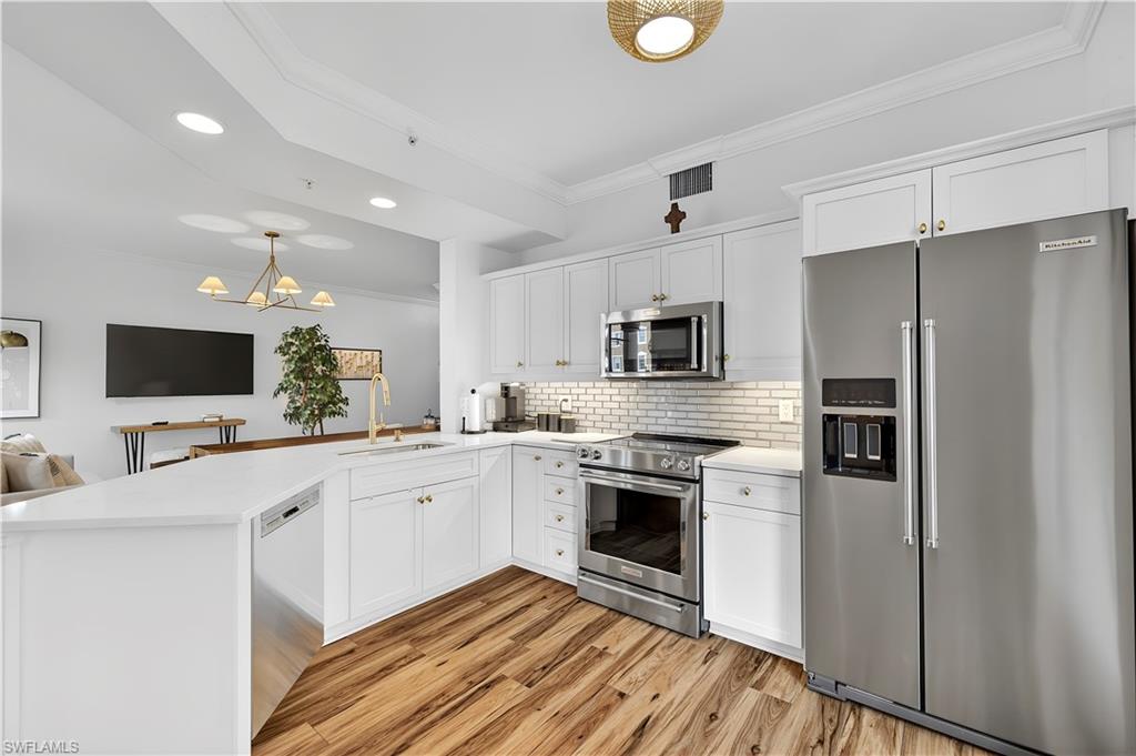 450 Bayfront Place, Unit 4202 Naples, FL 34102 - Photo 8 of 39 Kitchen with stainless steel appliances, white cabinetry, a peninsula, ornamental molding, and light wood finished floors