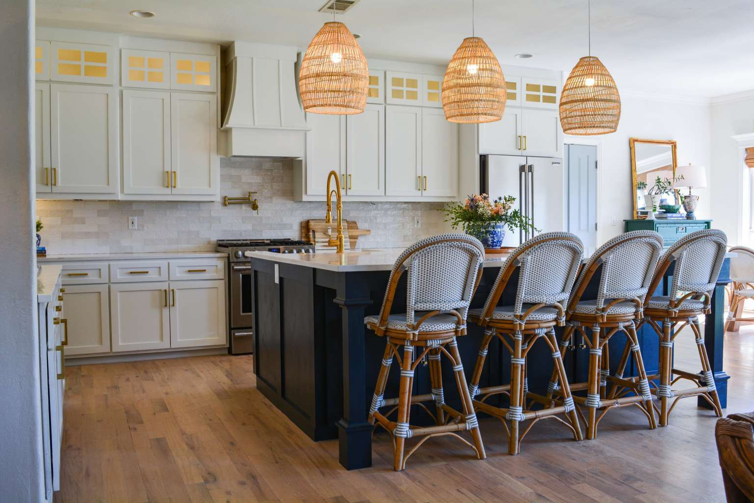 115 South Forest Ridge Boulevard Broken Arrow, OK 74014 - Photo 17 of 50 White cabinetry with gold-tone hardware, wood-finish flooring, a dark-toned kitchen island, tile backsplash, and three woven pendant light fixtures