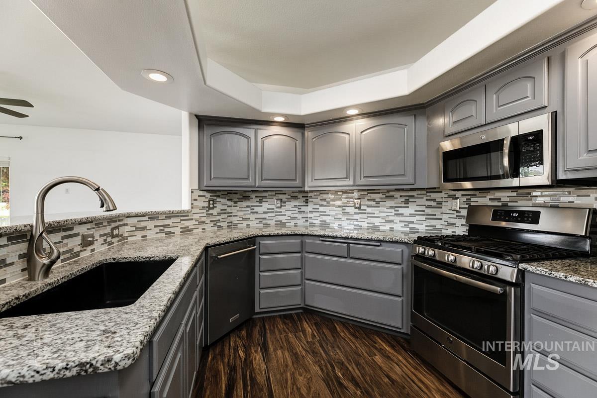 2575 S Bayou Meridian, ID 83642 - Photo 6 of 30 Kitchen featuring grey cabinetry, stainless steel appliances, speckled countertops, a tile backsplash, and wood-finish flooring