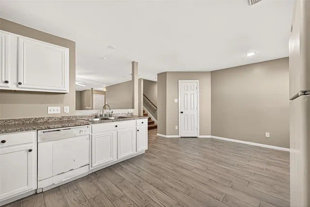 a large white kitchen with granite countertop a stove a sink and white cabinets with wooden floor
