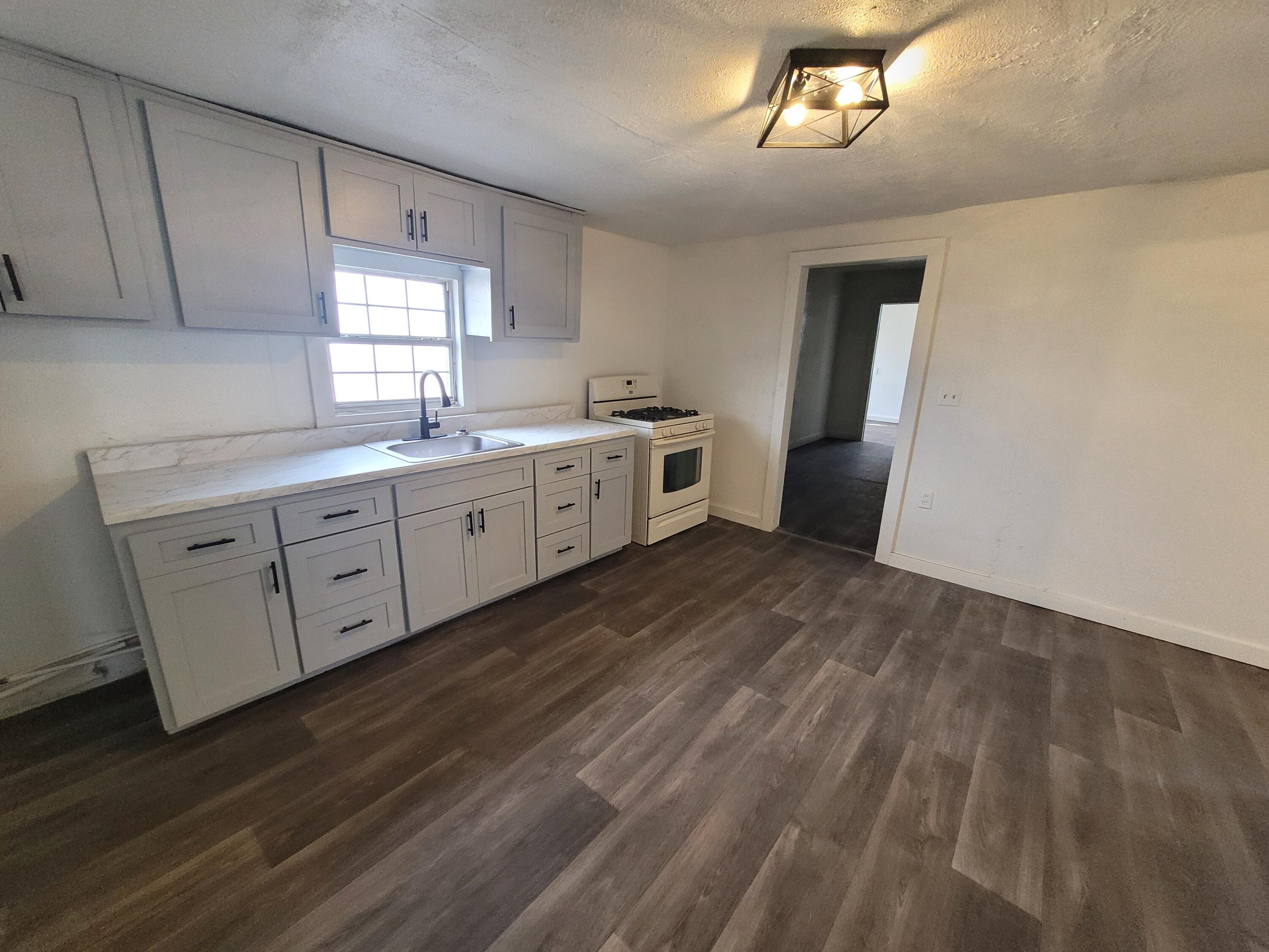 1055 South 3rd Street Slaton, TX 79364 - Photo 4 of 13 a large kitchen with a lot of white cabinets and wooden floor