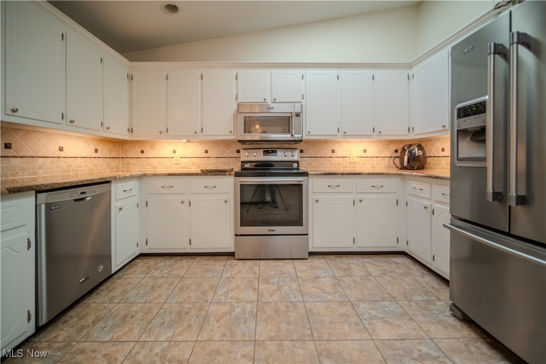 1394 Saxe Road Mogadore, OH 44260 - Photo 12 of 39 Kitchen featuring appliances with stainless steel finishes, light stone counters, tasteful backsplash, white cabinets, and vaulted ceiling
