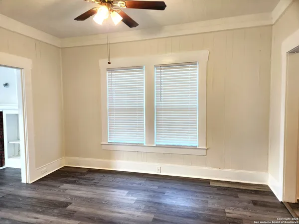 an empty room with wooden floor chandelier fan and windows