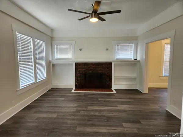 a view of an empty room with wooden floor fireplace and a window