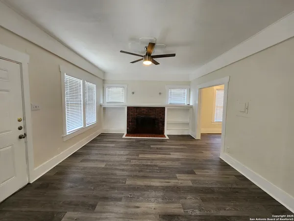 a view of a livingroom with a fireplace a ceiling fan and wooden floor