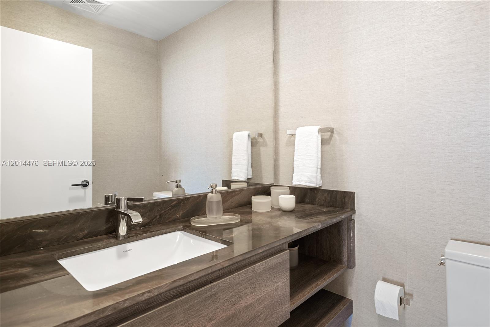 360 Ocean Drive, Unit 1106S Key Biscayne, FL 33149 - Photo 4 of 67 Powder Room – The powder room offers a streamlined vanity with a dark stone countertop, undermount sink, and wall-to-wall mirror. Textured wallcovering and open shelving add both style and function.