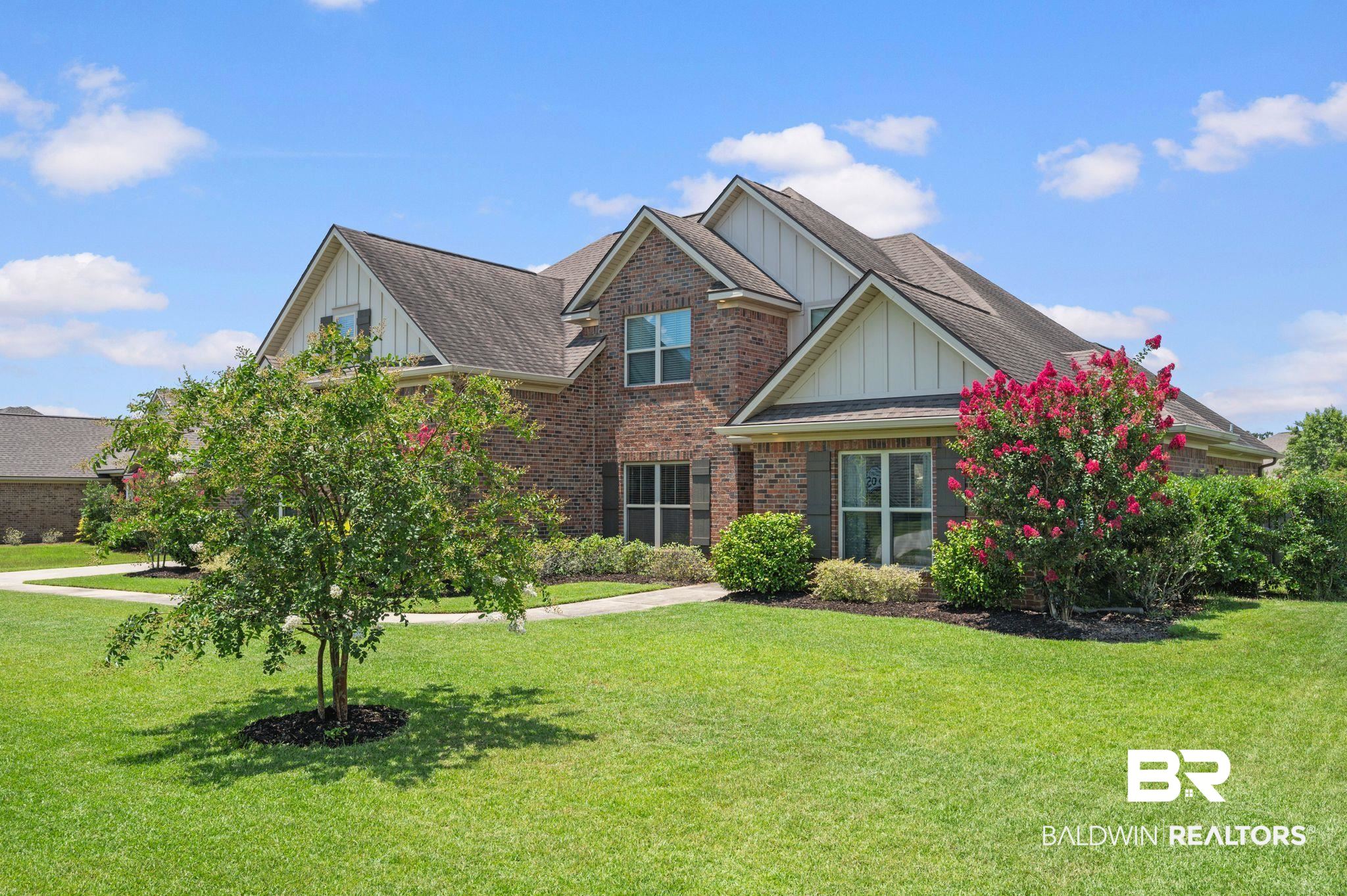 409 Fortune Drive Fairhope, AL 36532 - Photo 2 of 42 Brick exterior home featuring white siding gables, dark shingled roof, shuttered windows, and a manicured lawn with mature landscaping