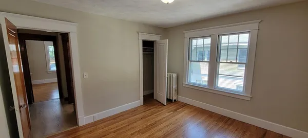 a view of an empty room with wooden floor and a window