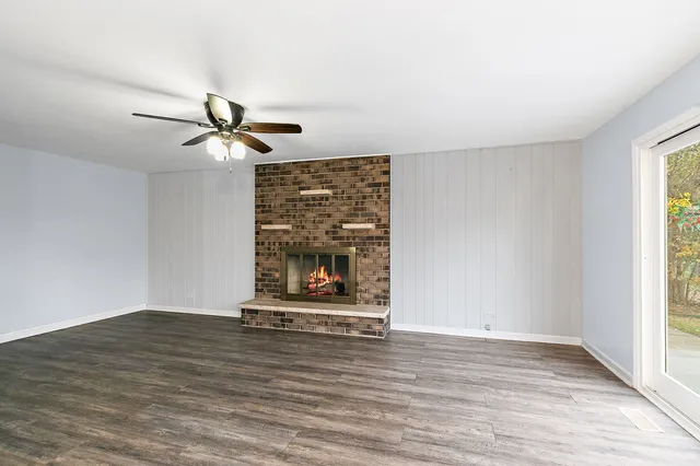 a view of a livingroom with a fireplace a ceiling fan and wooden floor