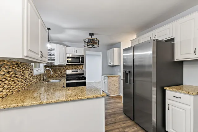 a kitchen with stainless steel appliances granite countertop a refrigerator a stove and a sink with wooden floor