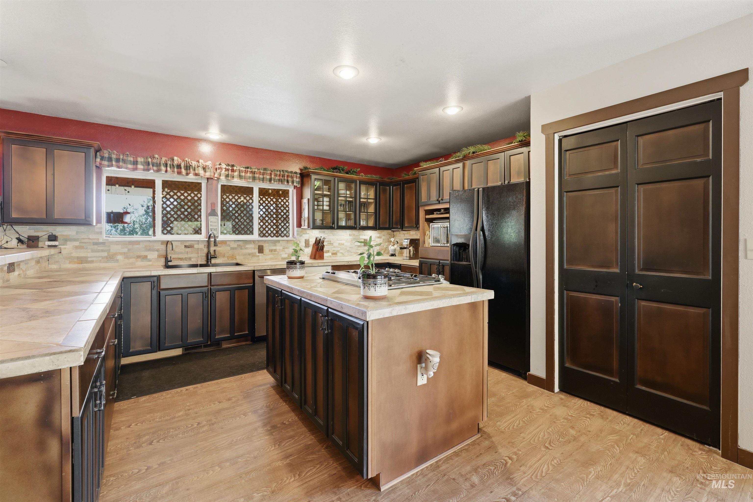 95 Johnson Creek Road Boise, ID 83716 - Photo 21 of 49 Kitchen with light wood-type flooring, a kitchen island, black fridge, glass fronted cabinets, and decorative backsplash