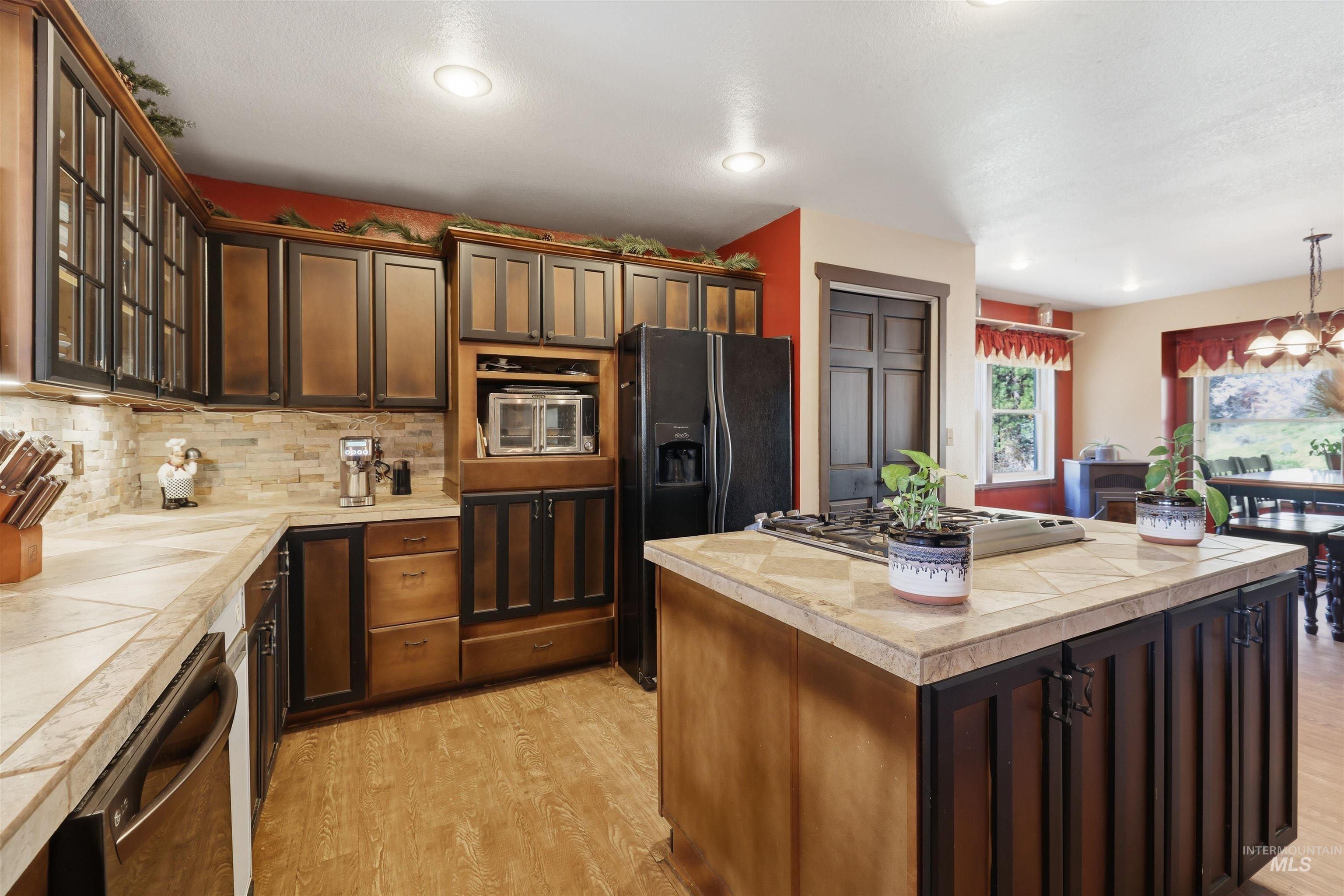 95 Johnson Creek Road Boise, ID 83716 - Photo 22 of 49 Kitchen featuring a kitchen island, dark wood finish cabinets, black refrigerator with ice dispenser, dishwasher, and light wood-style floors
