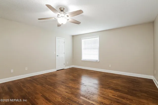 an empty room with wooden floor chandelier fan and windows