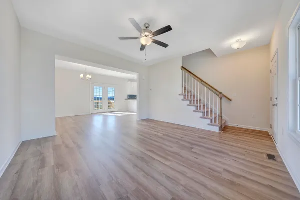 a view of an empty room with wooden floor and a ceiling fan