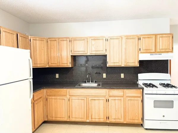 a kitchen with granite countertop a stove a sink and a refrigerator