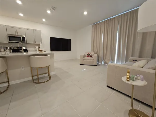 a living room with stainless steel appliances kitchen island furniture a couch a rug and a window