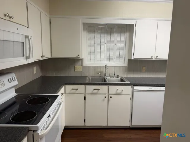 a kitchen with granite countertop white cabinets and a stove top oven