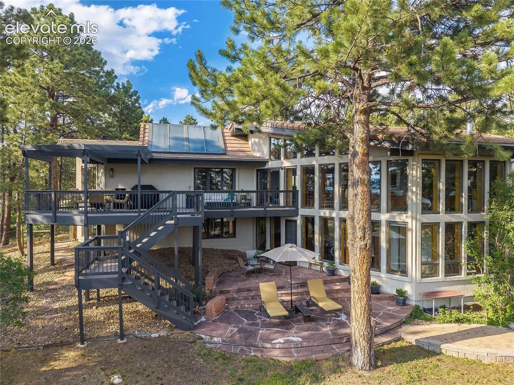 12730 Bridle Bit Road Colorado Springs, CO 80908 - Photo 40 of 50 Multi-level exterior featuring extensive window arrays, a spacious elevated deck with a pergola, and a flagstone patio with stone steps