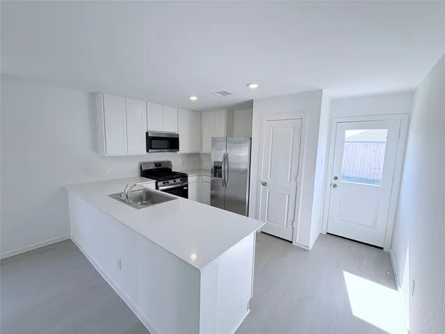 a kitchen with a sink a stove top oven a refrigerator a window and white cabinets