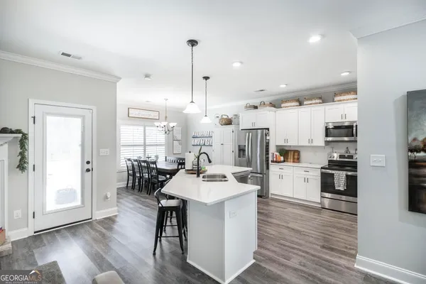 a kitchen with stainless steel appliances kitchen island granite countertop a dining table chairs and a refrigerator