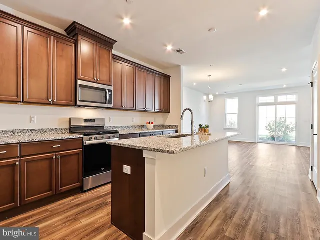 a kitchen with stainless steel appliances granite countertop wooden cabinets a stove top oven a sink and dishwasher with wooden floor