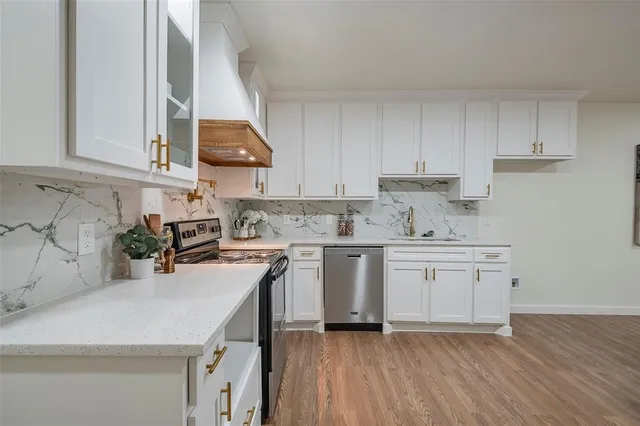 a kitchen with stainless steel appliances granite countertop a sink dishwasher stove and white cabinets with wooden floor