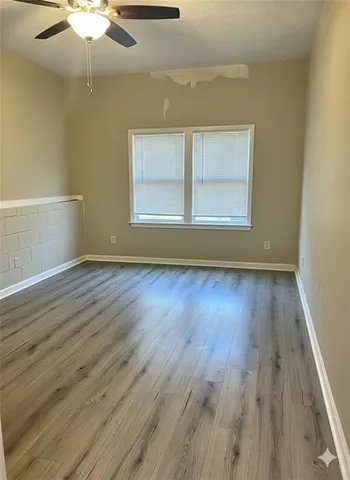 an empty room with wooden floor chandelier fan and windows