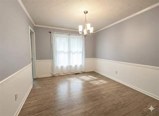 an empty room with wooden floor chandelier and windows