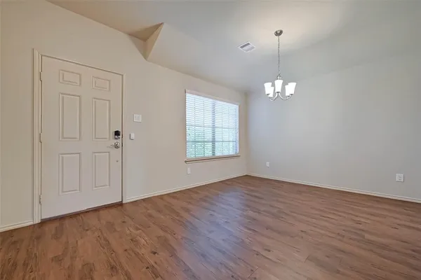 an empty room with wooden floor chandelier and window