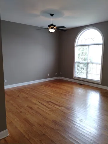 an empty room with wooden floor chandelier and windows